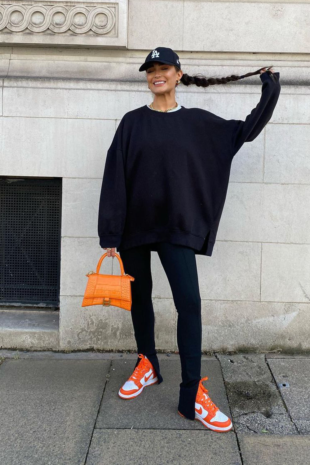 boné no look all black com moletom oversized, calça preta flire, tênis e bolsa laranja