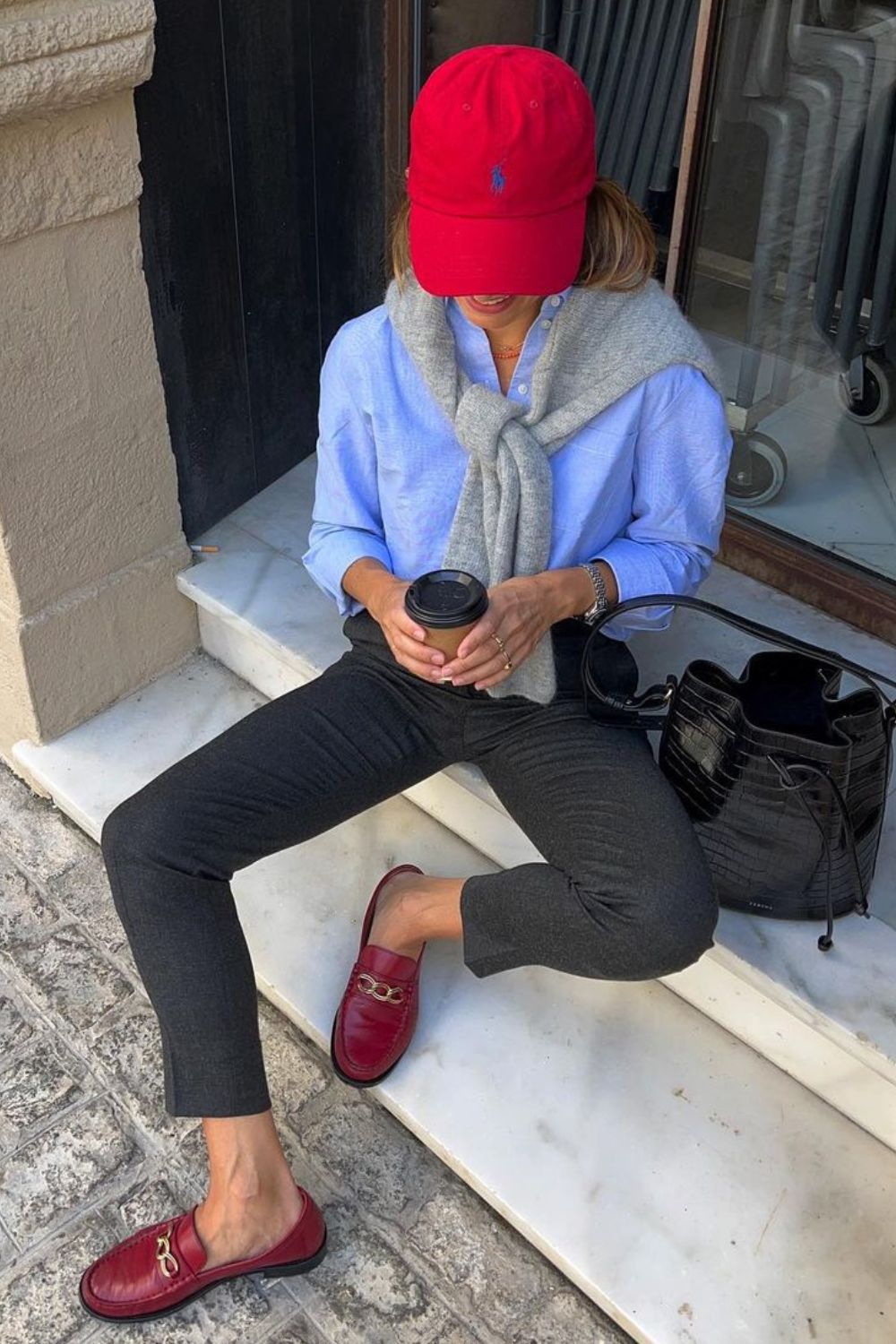 Ponto vermelho no look, boné, camisa azul, calça preta, loafer e bucket bag