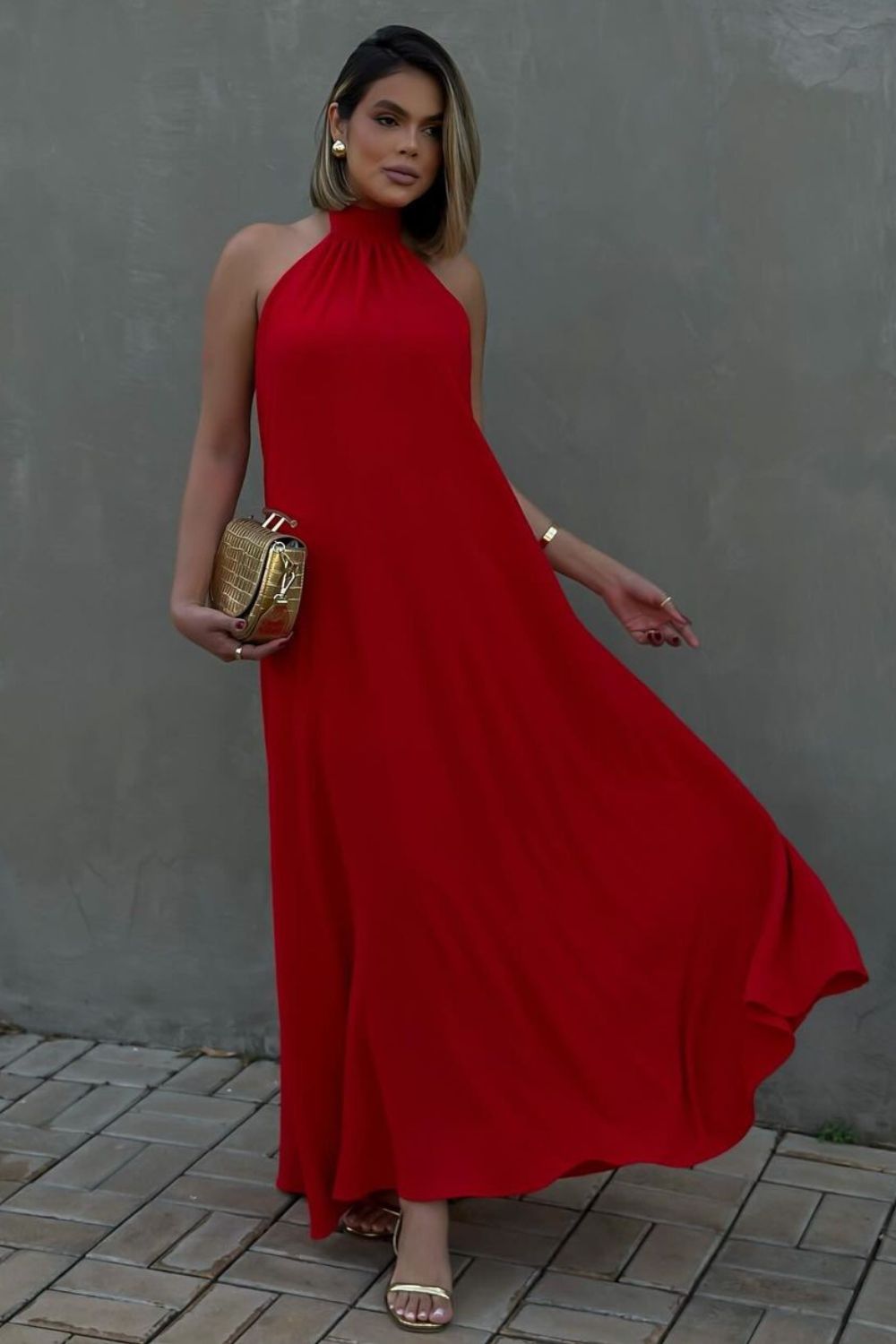 Look elegante com vestido vermelho longo de gola alta, bolsa dourada, sandália de tiras dourada e acessórios dourados