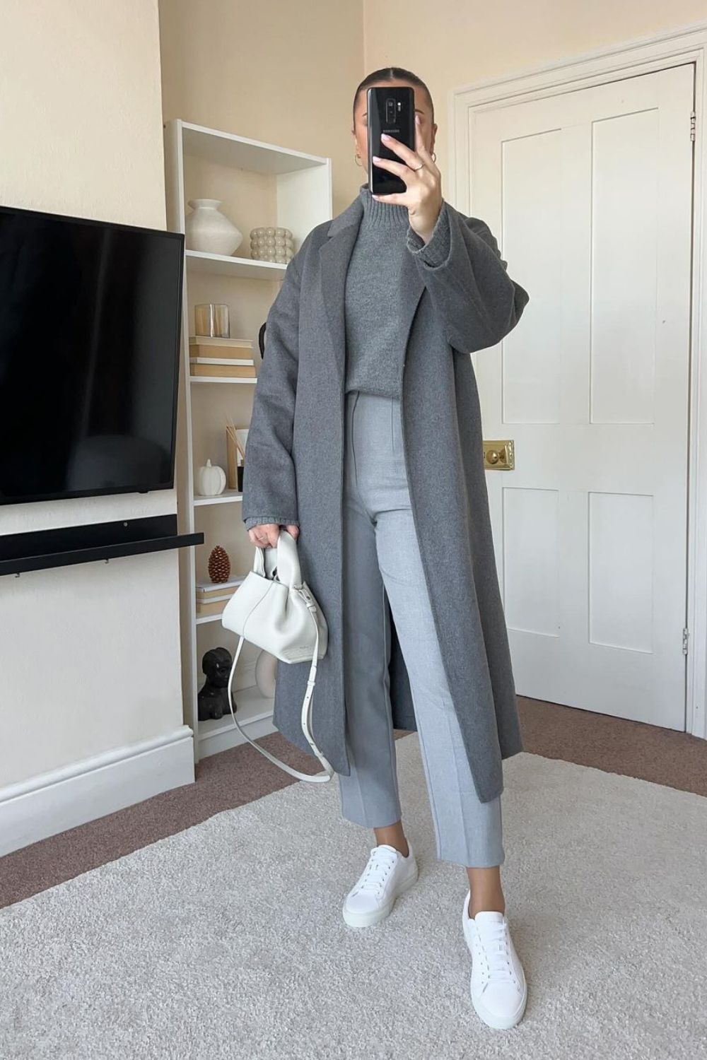 Suéter cinza de gola alta, sobretudo, calça de alfaiataria cinza, tênis e bolsa branca