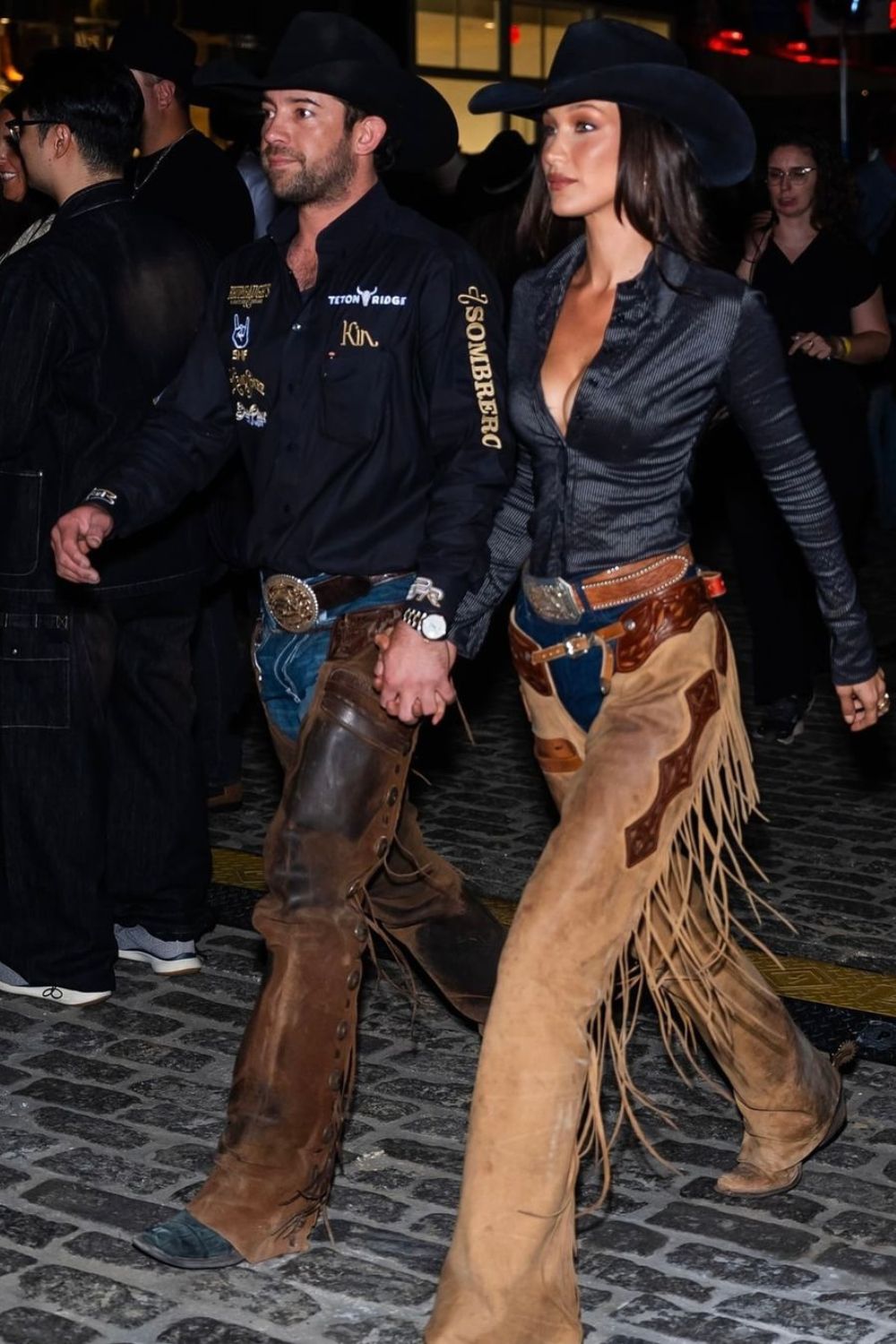 Bella Hadid com o namorado vaqueiro. Chapéu de cowgirl, camisa preta, calça jeans com chaparreira, cinto de fivela e sapato de camurça