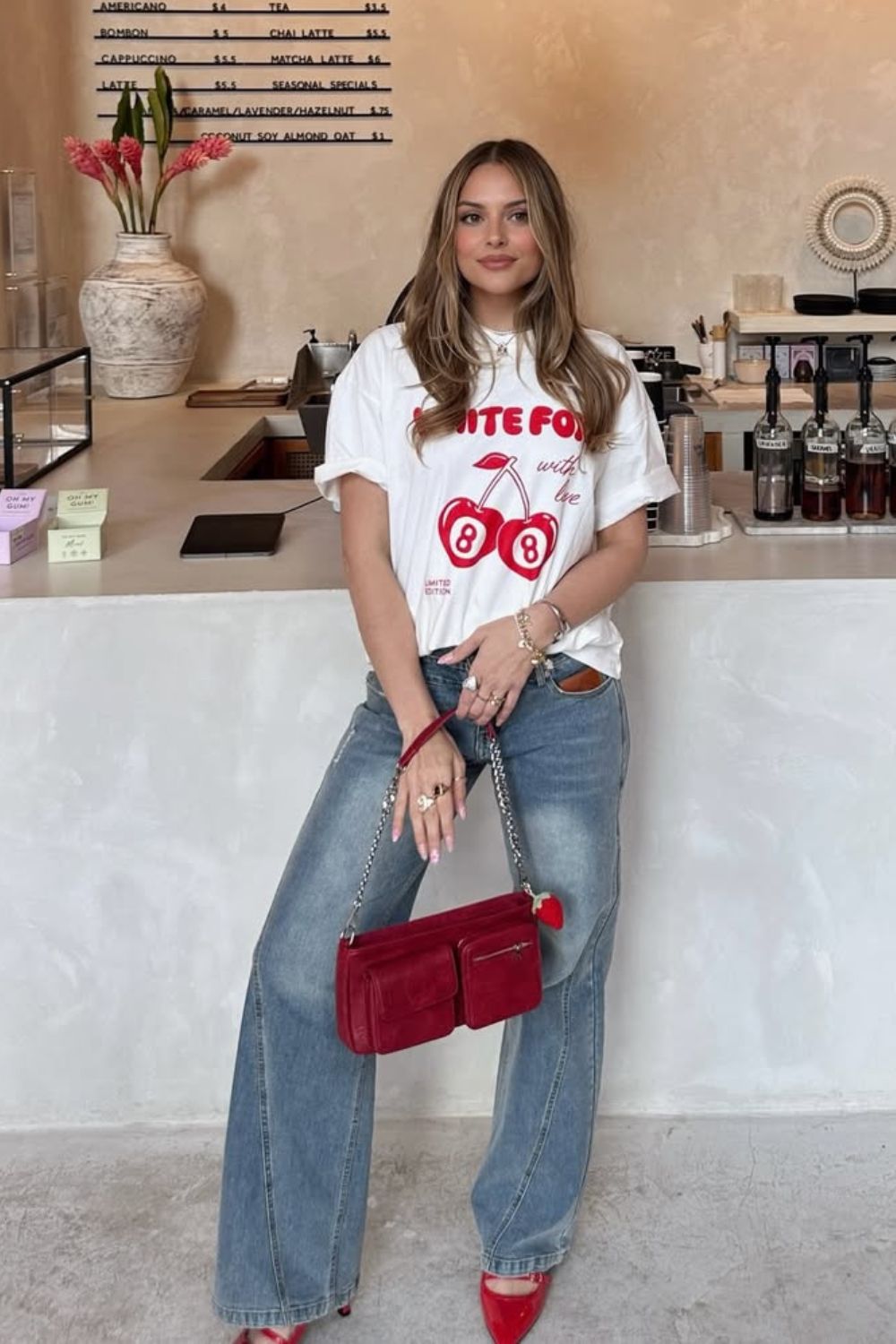 T-shirt branca com estampa vermelha, calça jeans com lavagem anos 2000, sapato de bico fino e bolsa vermelha