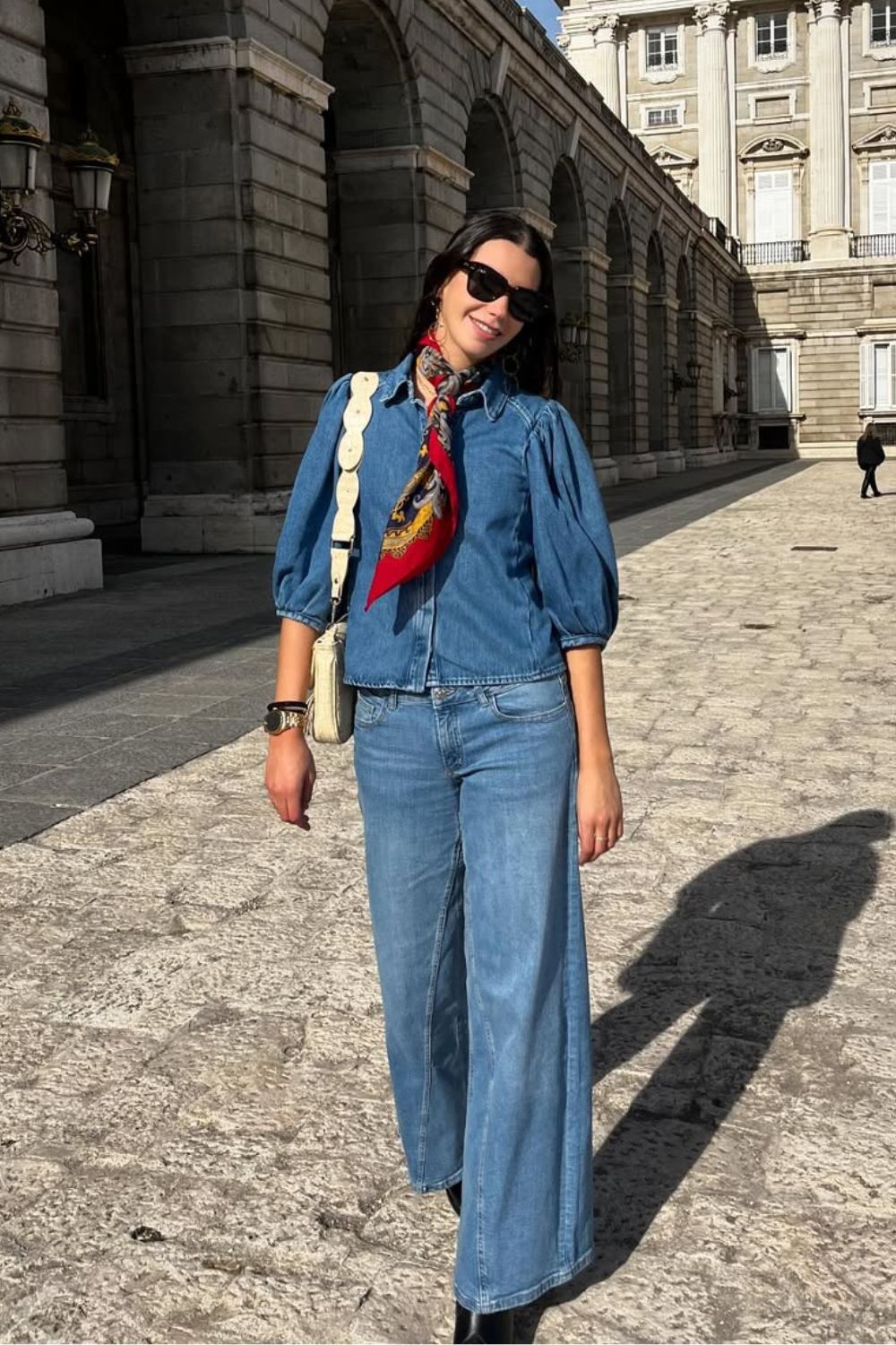 Look jeans com jeans, com mamisa de manga e calça wide leg, como acessórios: cinto no pescoço e bolsa bege