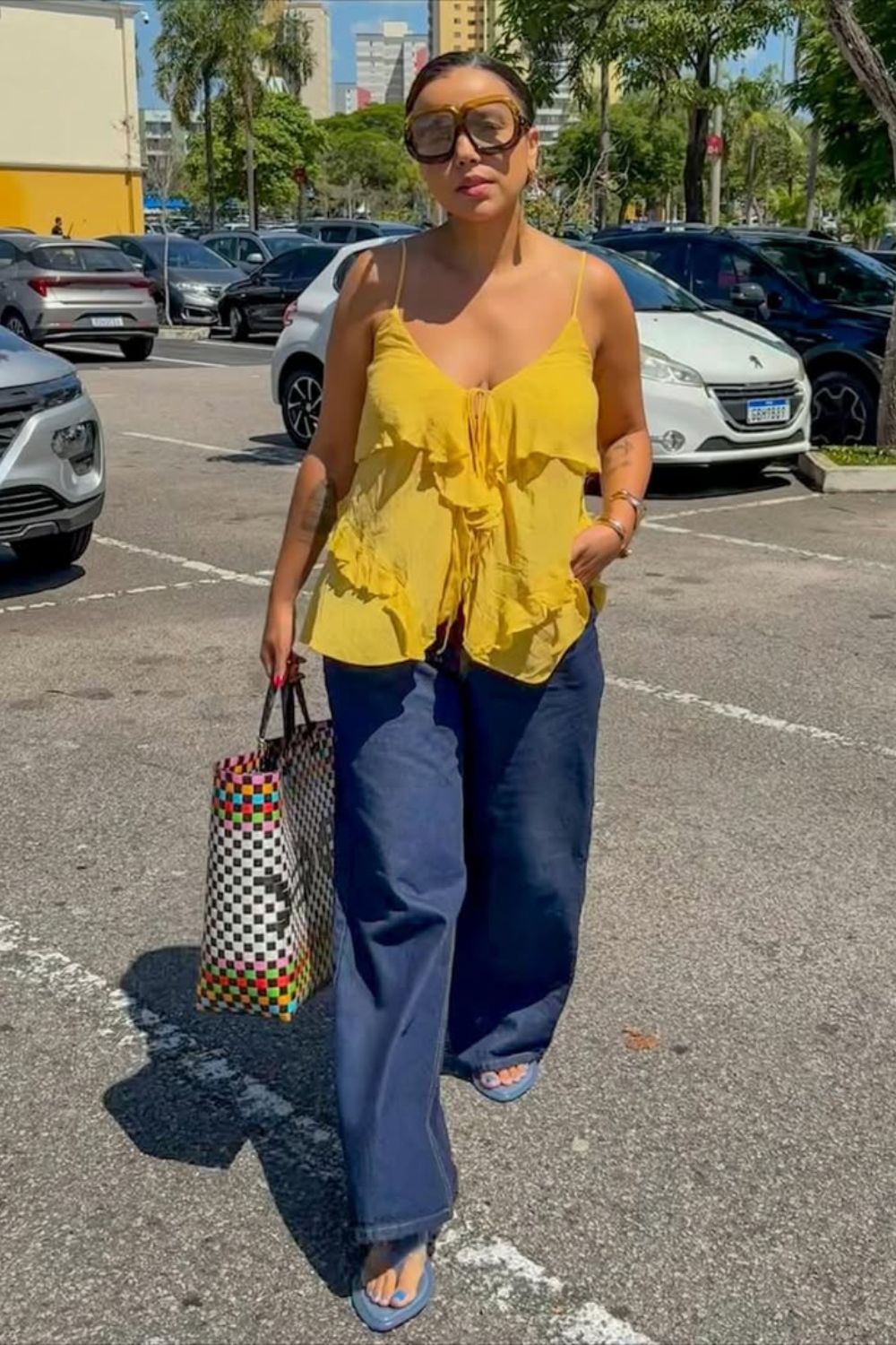 calça jeans, top laranja com babados, sandália azul e maxi bolsa com estampa xadrez