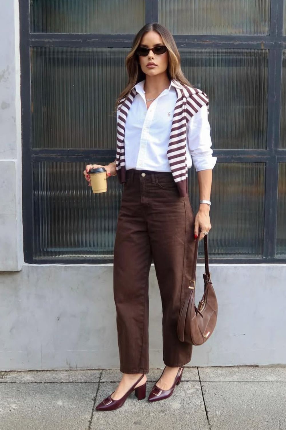 O poder das estampas num look preppy com camisa branca, suéter jogadinho sobre os ombros e calça marrom