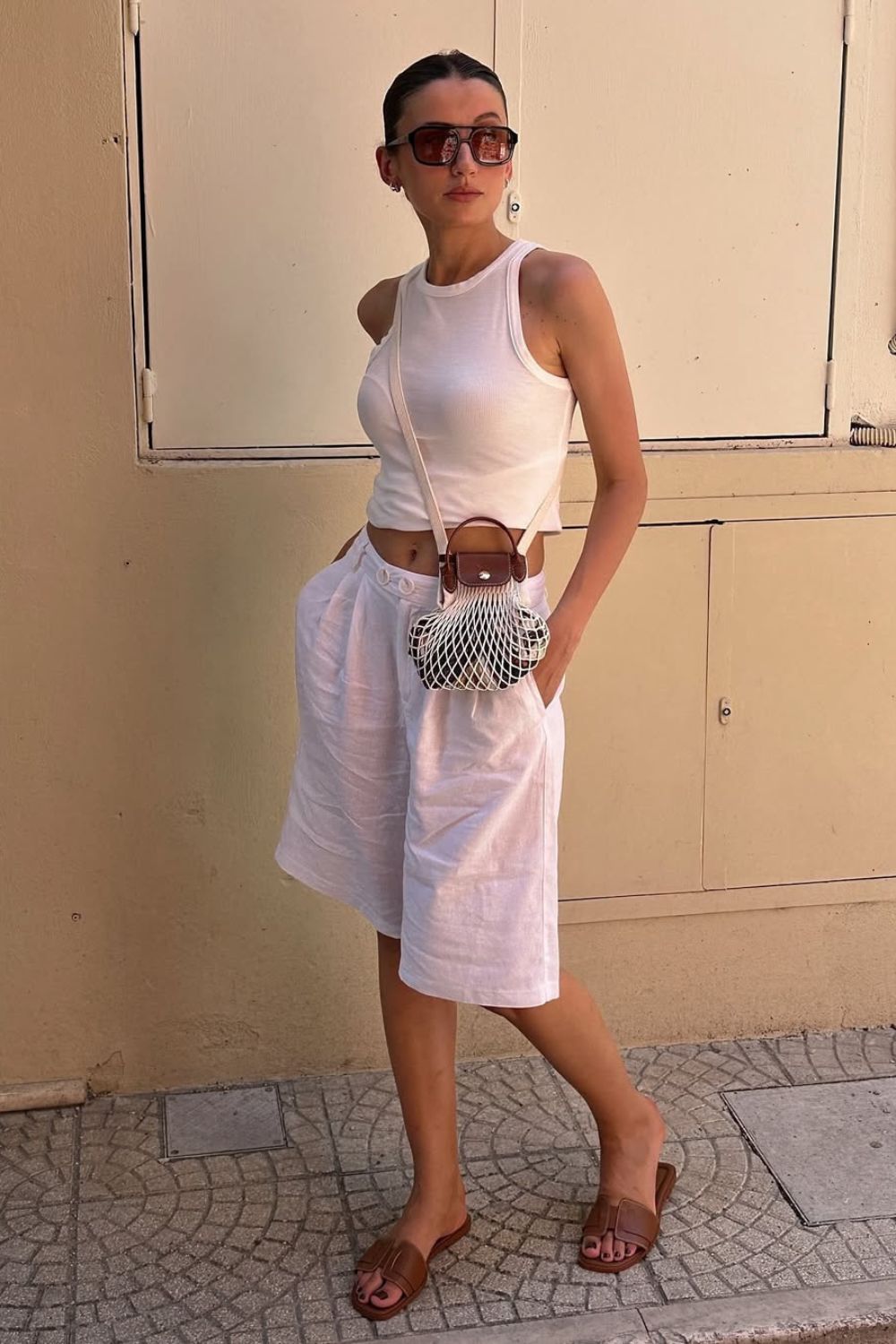 Look casual com Regata branca e jorts branca e rasteirinha. Como acessórios, bolsa de rede e óculos escuros.