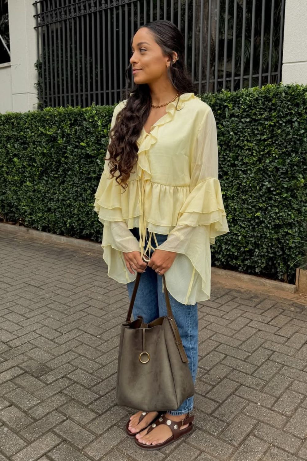 Blusa amarela de babados, calça jeans, rasteirinha e bucket bag