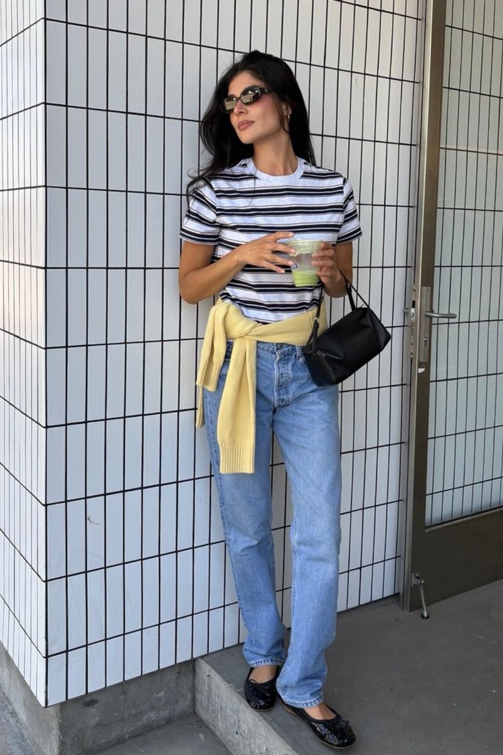 Blusa listrada, calça jeans reta e suéter amarelo preso na cintura, sapatilha preta e mini bolsa