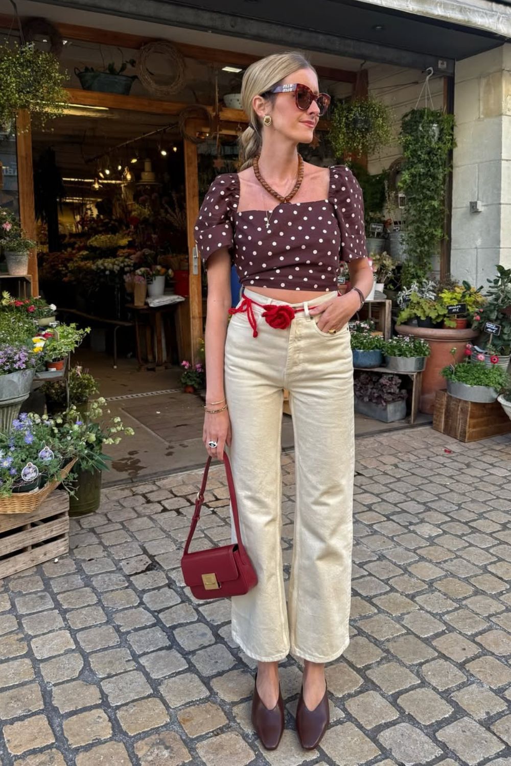 Cropped marrom de estampa poá, calça caqui com cinto vermelho com maxi rosa