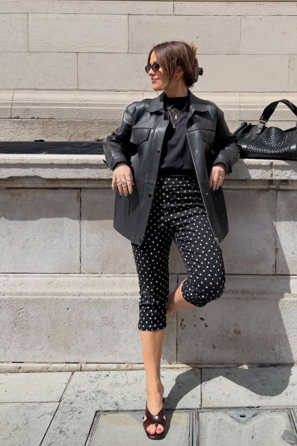 Jaqueta de couro, blusa preta e calça capri com estampa de bolinhas